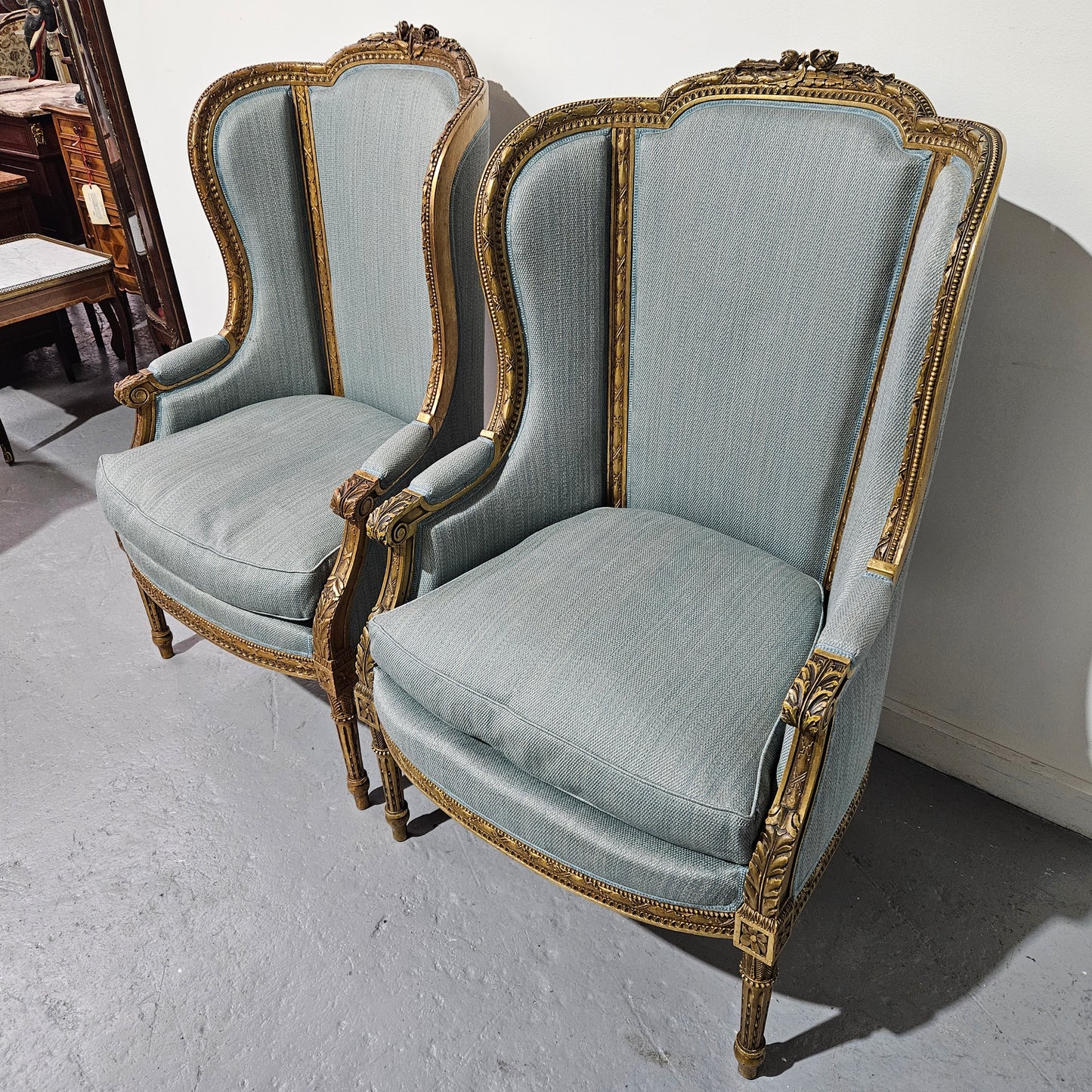 Lovely pair of Louis 16th style gilt & upholstered wingback bergeres with two comfortable cushions. These chairs are in good original condition. Please view photos as they form part of the description.