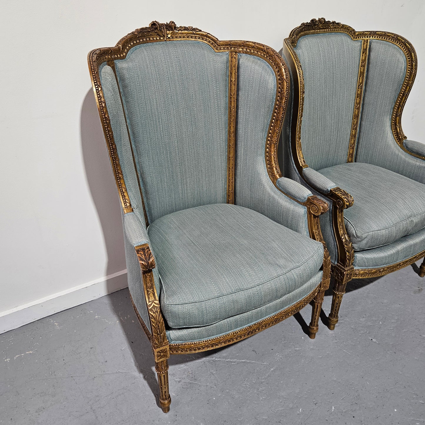 Lovely pair of Louis 16th style gilt & upholstered wingback bergeres with two comfortable cushions. These chairs are in good original condition. Please view photos as they form part of the description.