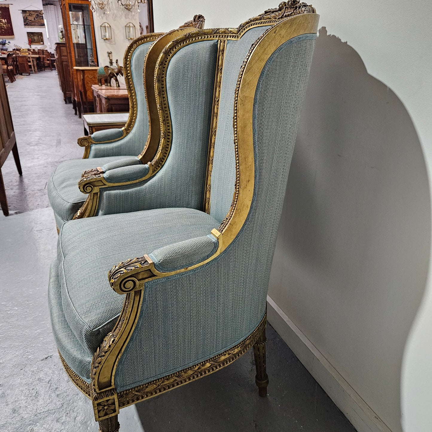 Lovely pair of Louis 16th style gilt & upholstered wingback bergeres with two comfortable cushions. These chairs are in good original condition. Please view photos as they form part of the description.