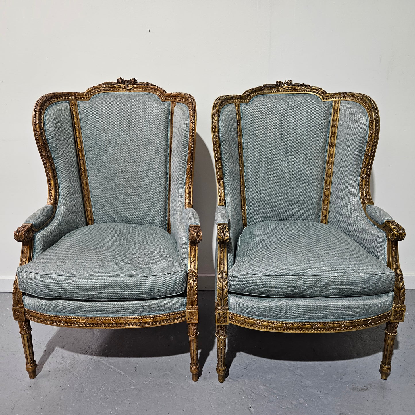 Lovely pair of Louis 16th style gilt & upholstered wingback bergeres with two comfortable cushions. These chairs are in good original condition. Please view photos as they form part of the description.