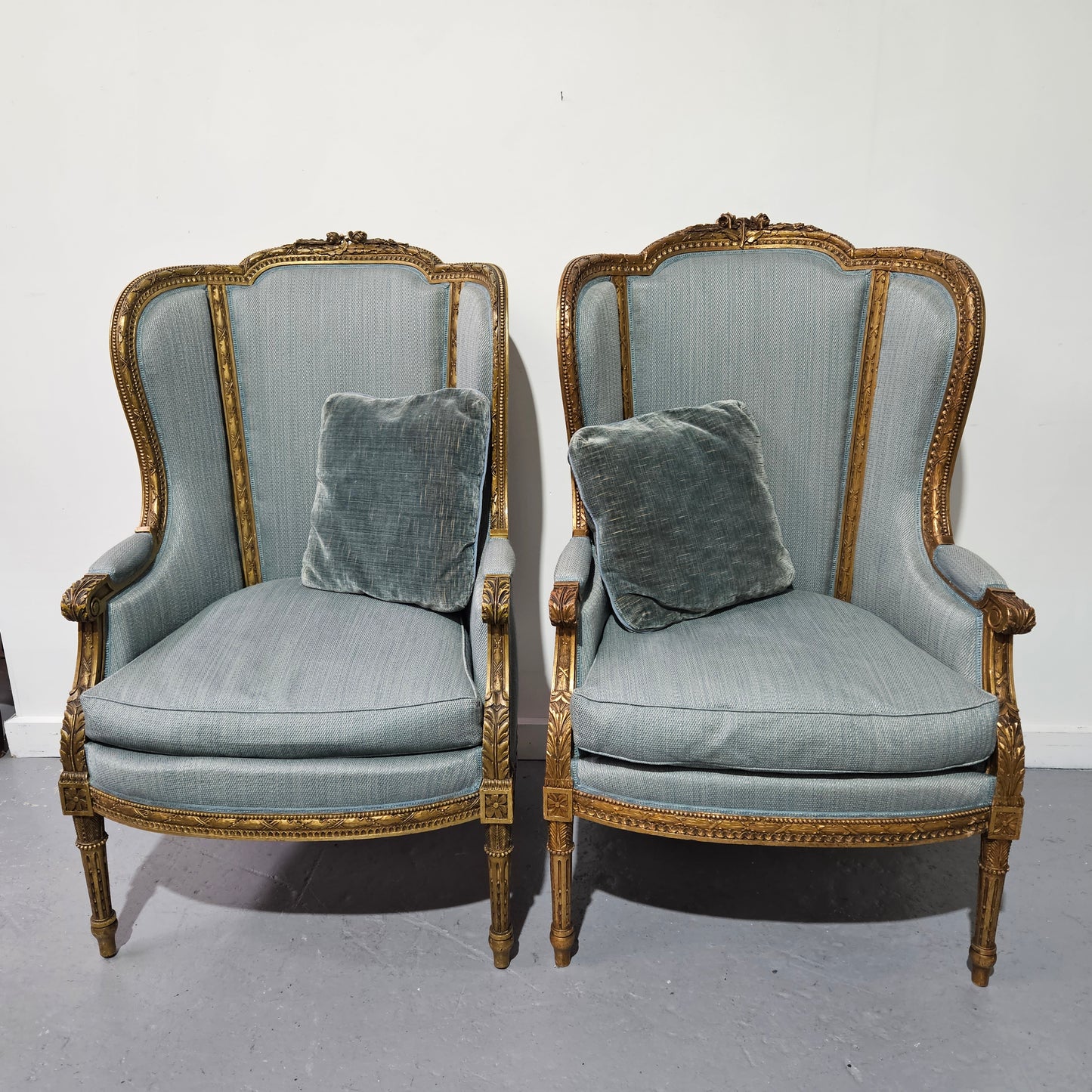 Lovely pair of Louis 16th style gilt & upholstered wingback bergeres with two comfortable cushions. These chairs are in good original condition. Please view photos as they form part of the description.