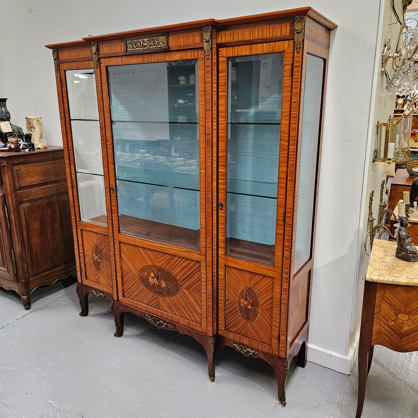Elegant three door Louis XV transitional style vitrine with decorative bronze mounts. This unit has two glass shelves and one wooden shelf providing plenty of storage. It is in great original detailed condition. Please see the photos as they form part of the description.