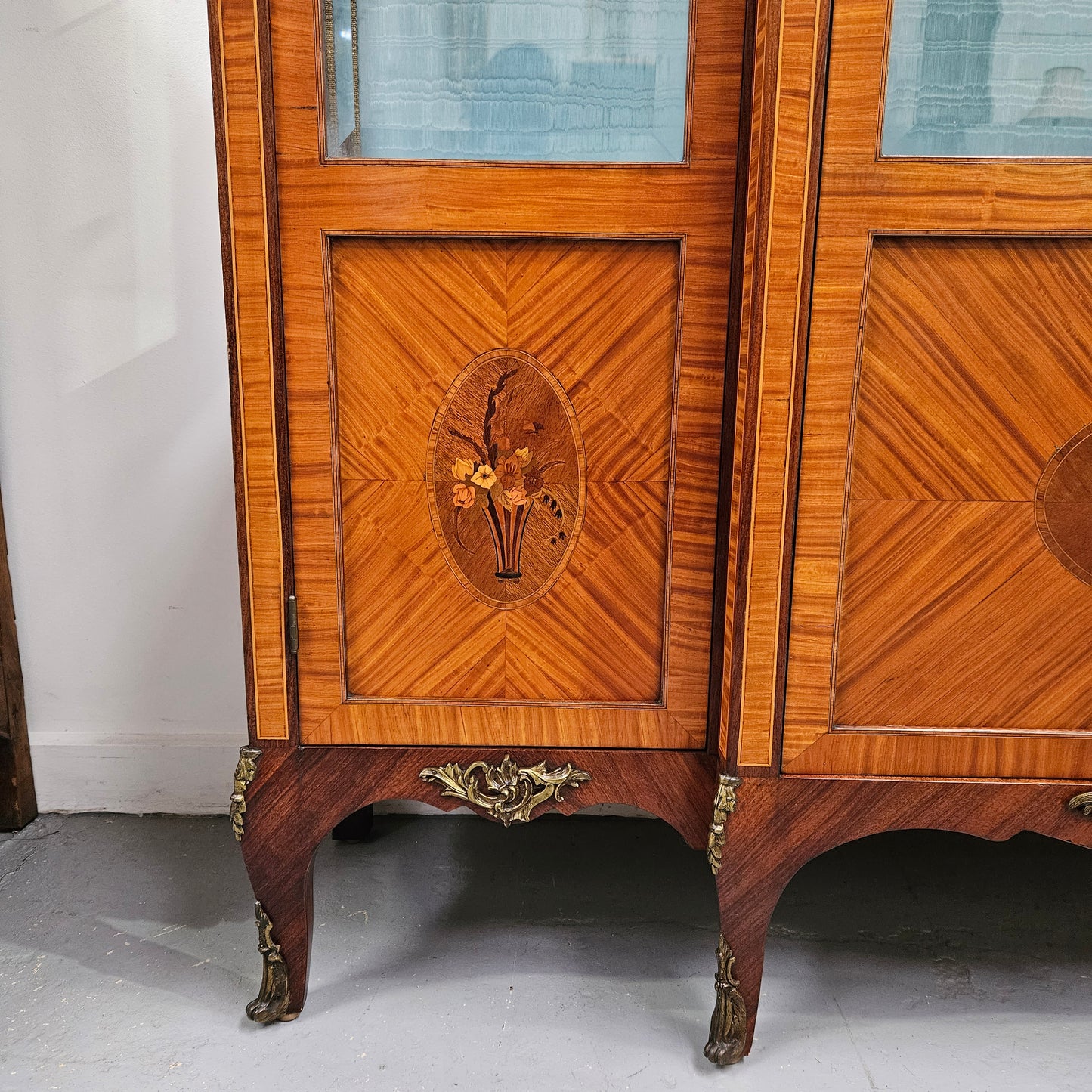 Elegant three door Louis XV transitional style vitrine with decorative bronze mounts. This unit has two glass shelves and one wooden shelf providing plenty of storage. It is in great original detailed condition. Please see the photos as they form part of the description.