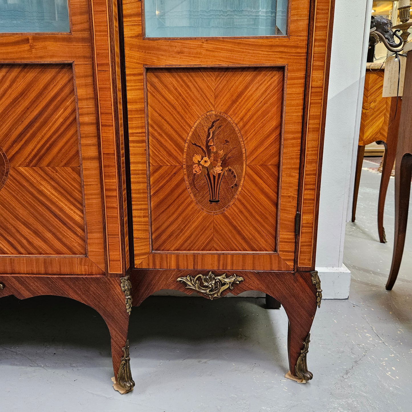 Elegant three door Louis XV transitional style vitrine with decorative bronze mounts. This unit has two glass shelves and one wooden shelf providing plenty of storage. It is in great original detailed condition. Please see the photos as they form part of the description.