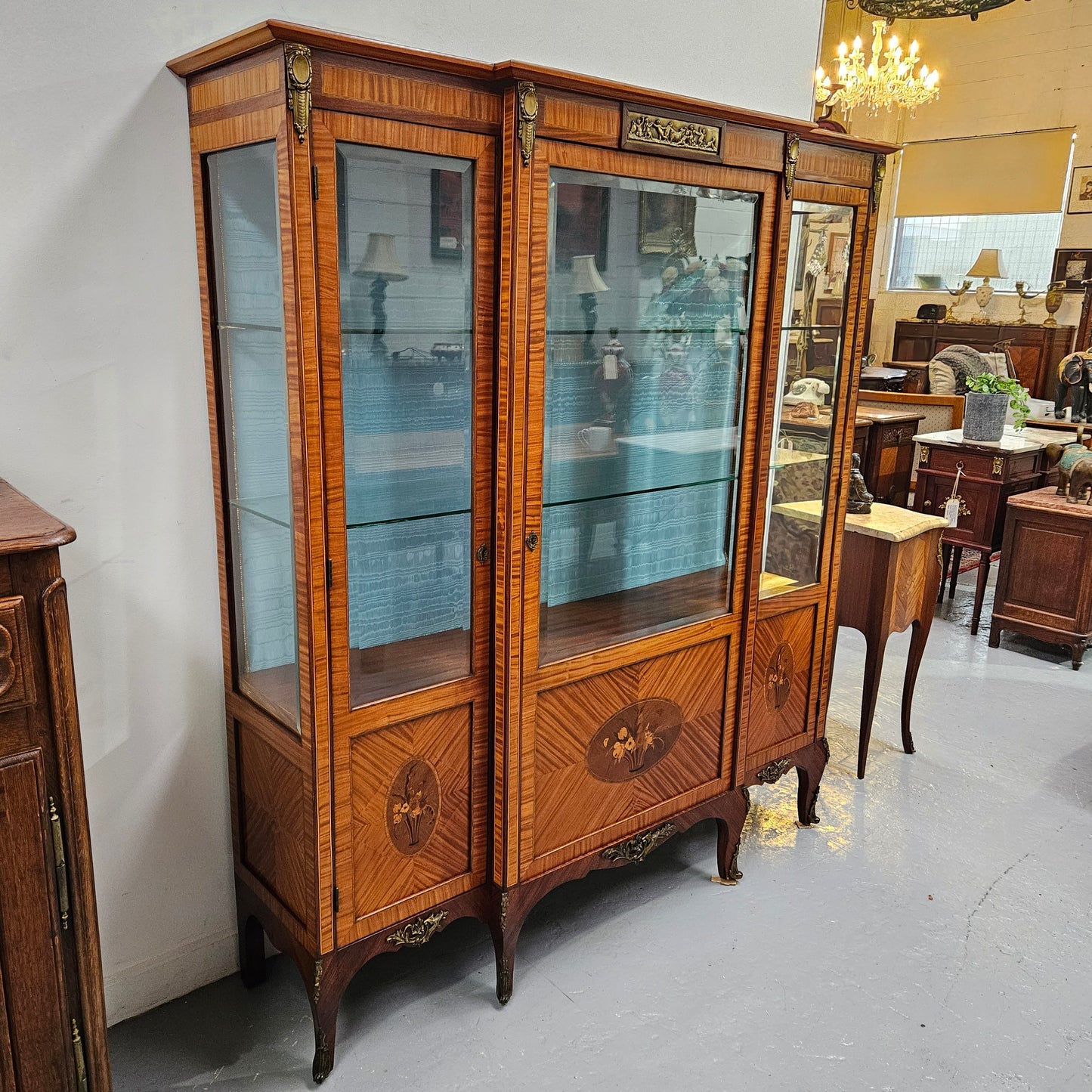 Elegant three door Louis XV transitional style vitrine with decorative bronze mounts. This unit has two glass shelves and one wooden shelf providing plenty of storage. It is in great original detailed condition. Please see the photos as they form part of the description.