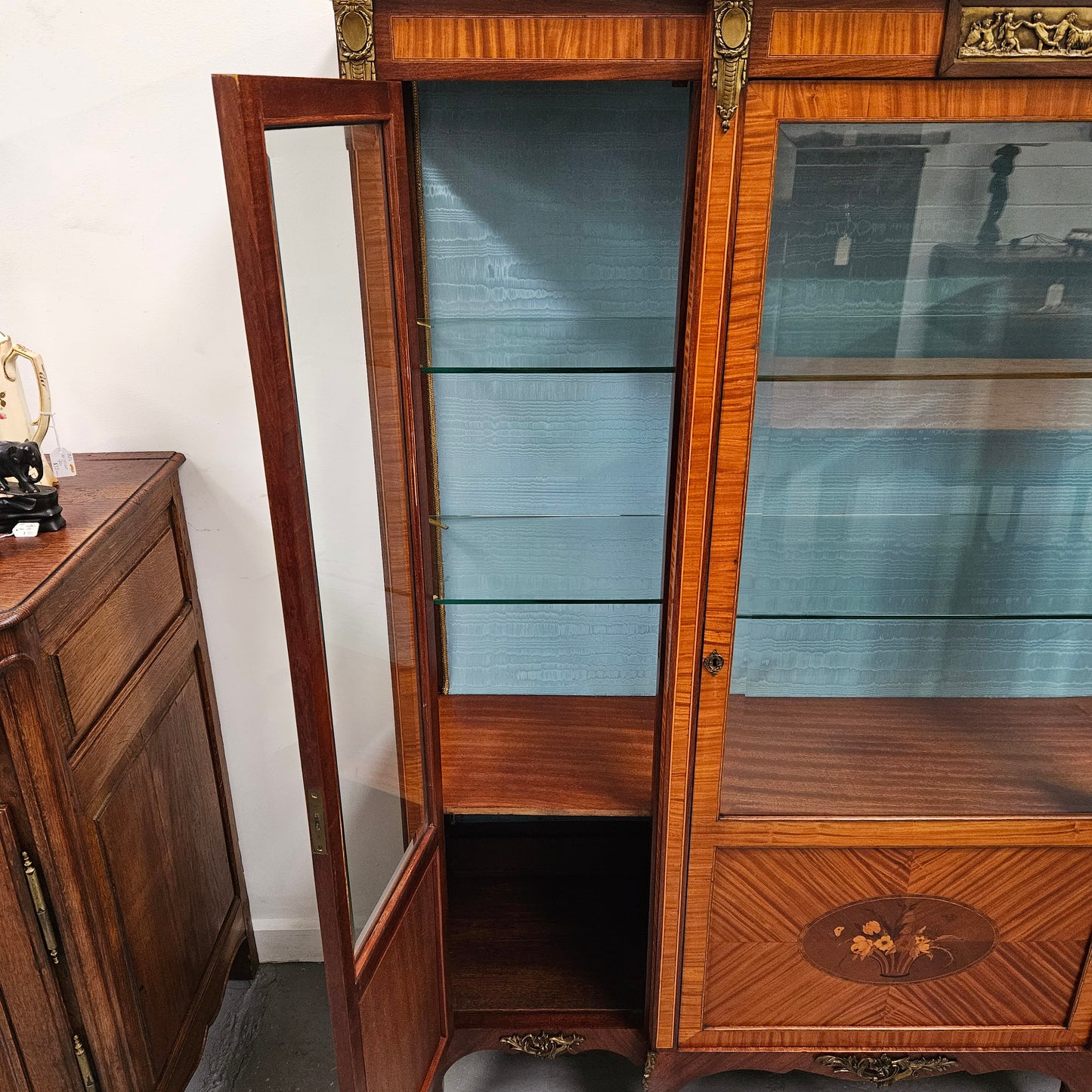 Elegant three door Louis XV transitional style vitrine with decorative bronze mounts. This unit has two glass shelves and one wooden shelf providing plenty of storage. It is in great original detailed condition. Please see the photos as they form part of the description.