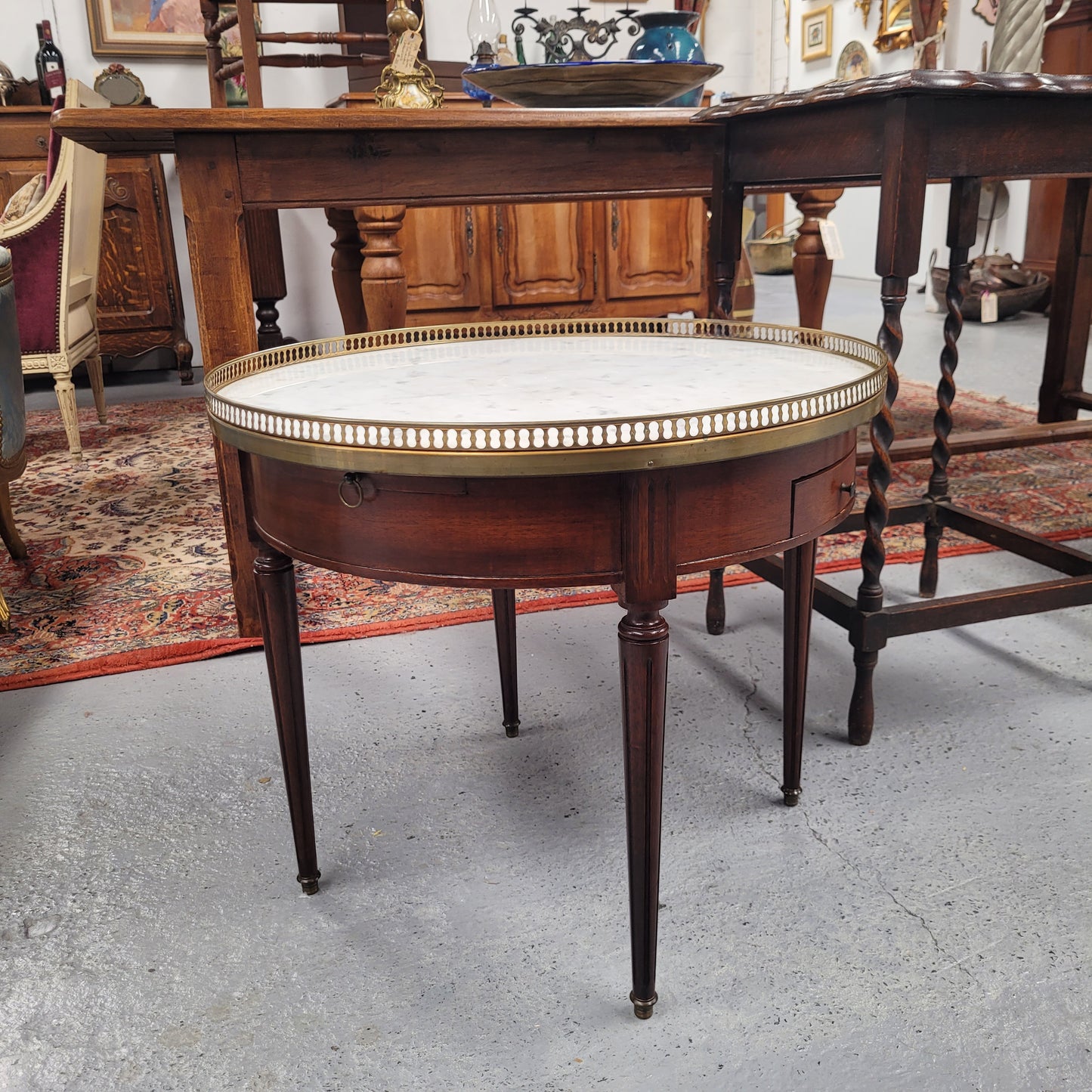 French Louis XVI style Mahogany Bouillotte table, featuring original white Carrara marble top finished nicely with a gilt brass gallery and standing on elegant tapered and fluted legs. It consists of two drawers and two slide-out extensions with leather inserts. Sourced from France and in good original detailed condition. Circa 1930.