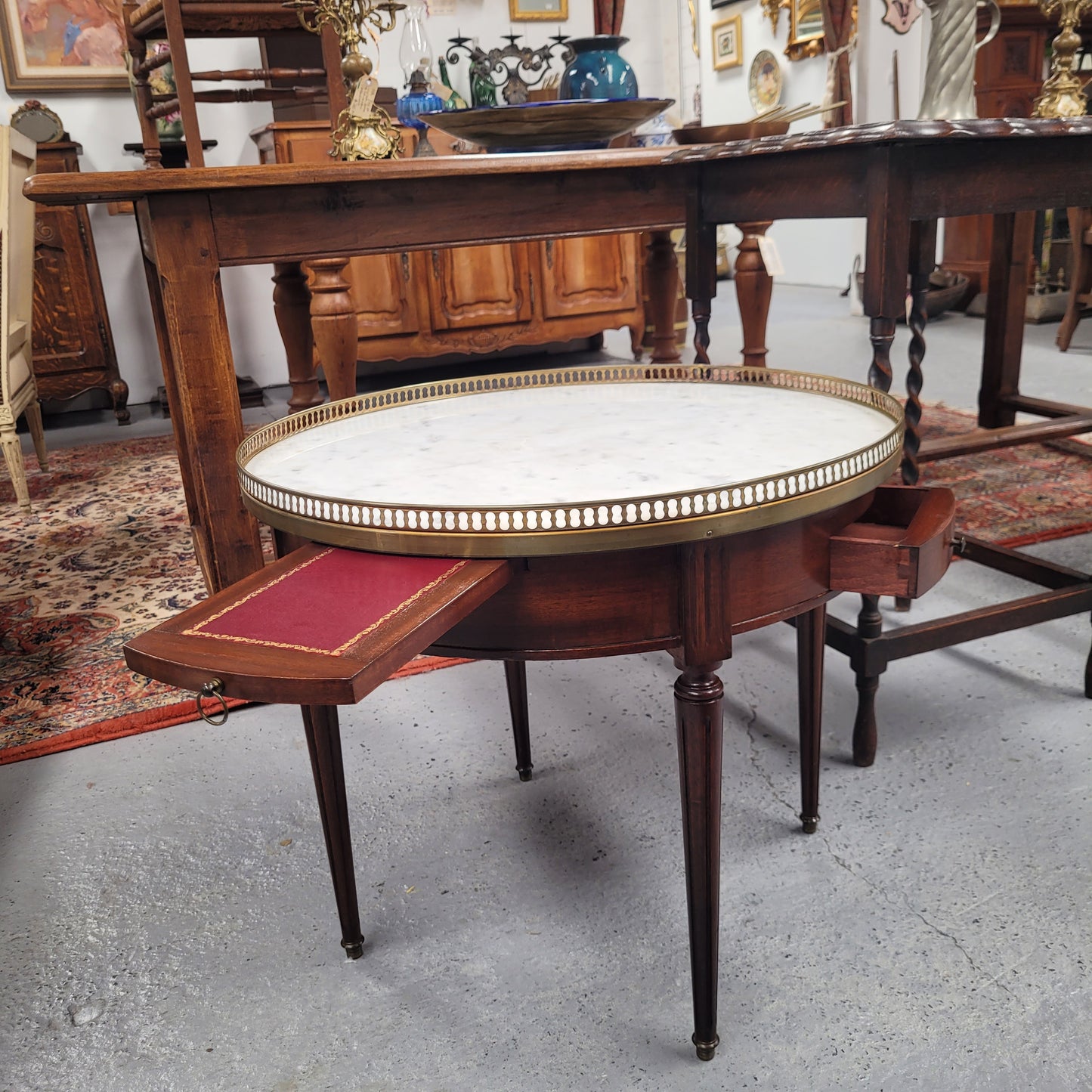 French Louis XVI style Mahogany Bouillotte table, featuring original white Carrara marble top finished nicely with a gilt brass gallery and standing on elegant tapered and fluted legs. It consists of two drawers and two slide-out extensions with leather inserts. Sourced from France and in good original detailed condition. Circa 1930.