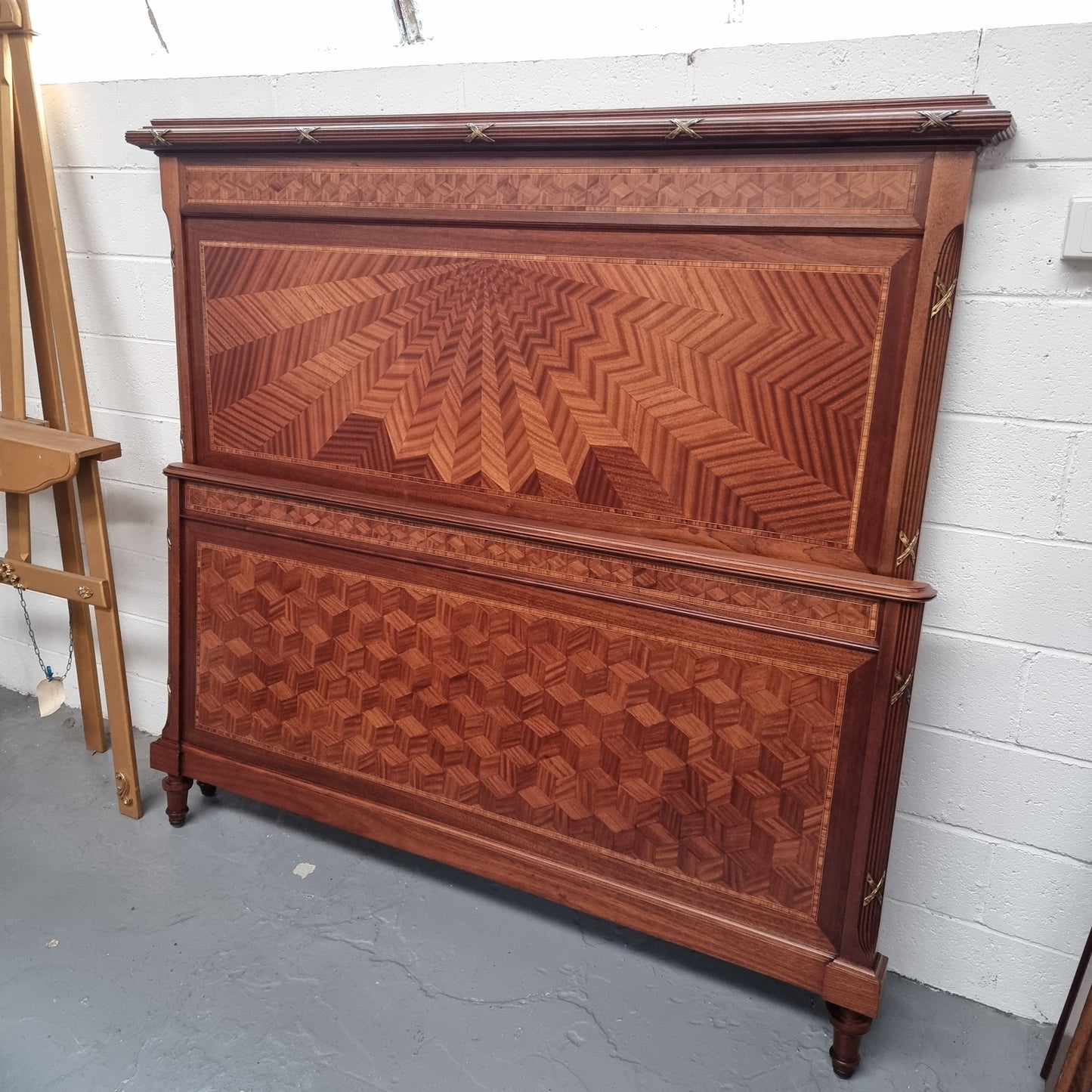 French Louis XVI queen-size bed. The headboard and footboard feature geometric cube shaped parquet pattern panels and decorative mounts. It comes with beautiful side rails and custom made slates meaning once set up all you simply need to do is place your mattress on top. It has been sourced directly from France and is in good original detailed condition.