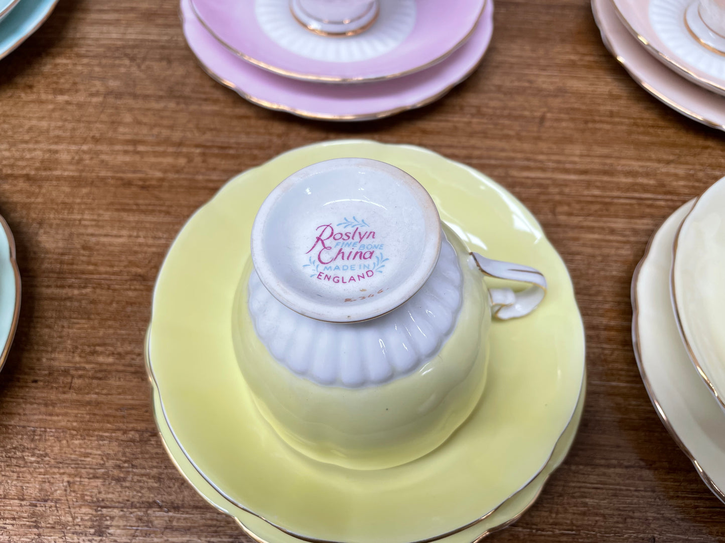 A set of six vintage Roslyn fine bone china trios in pink, turquoise, yellow, and green, displayed on a wooden surface.