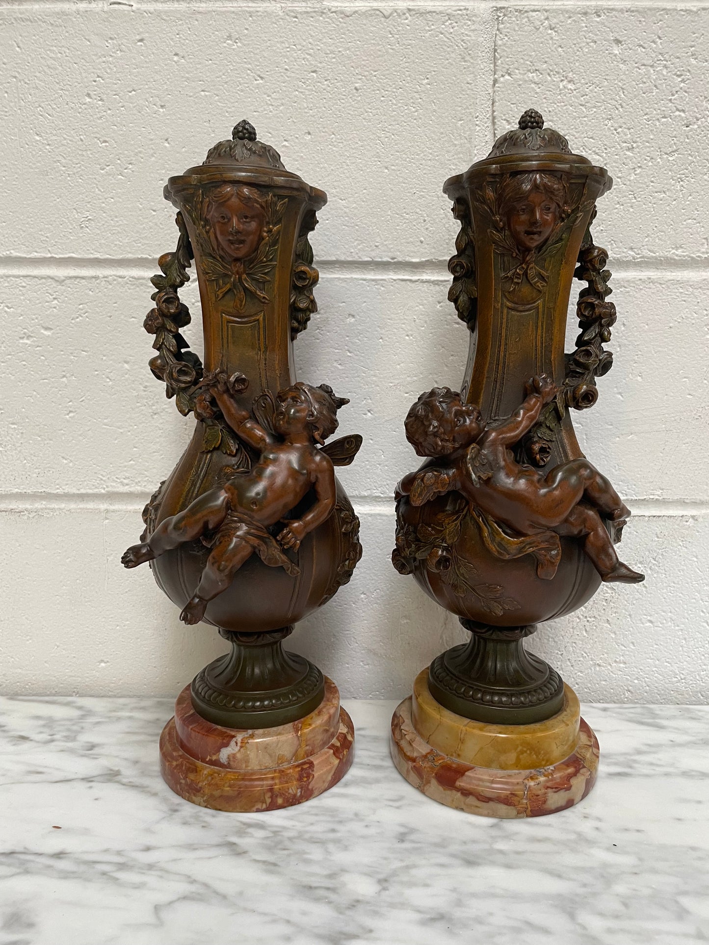 Pair of French Bronzed Metal Cherub Urns on a Marble Base