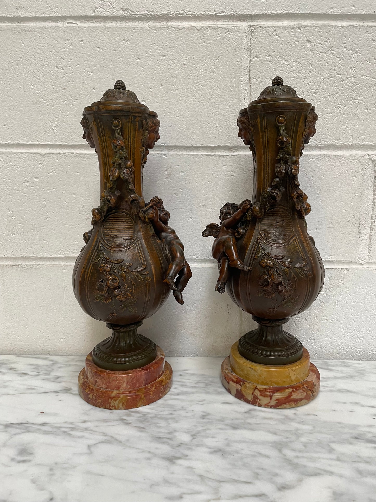 Pair of French Bronzed Metal Cherub Urns on a Marble Base