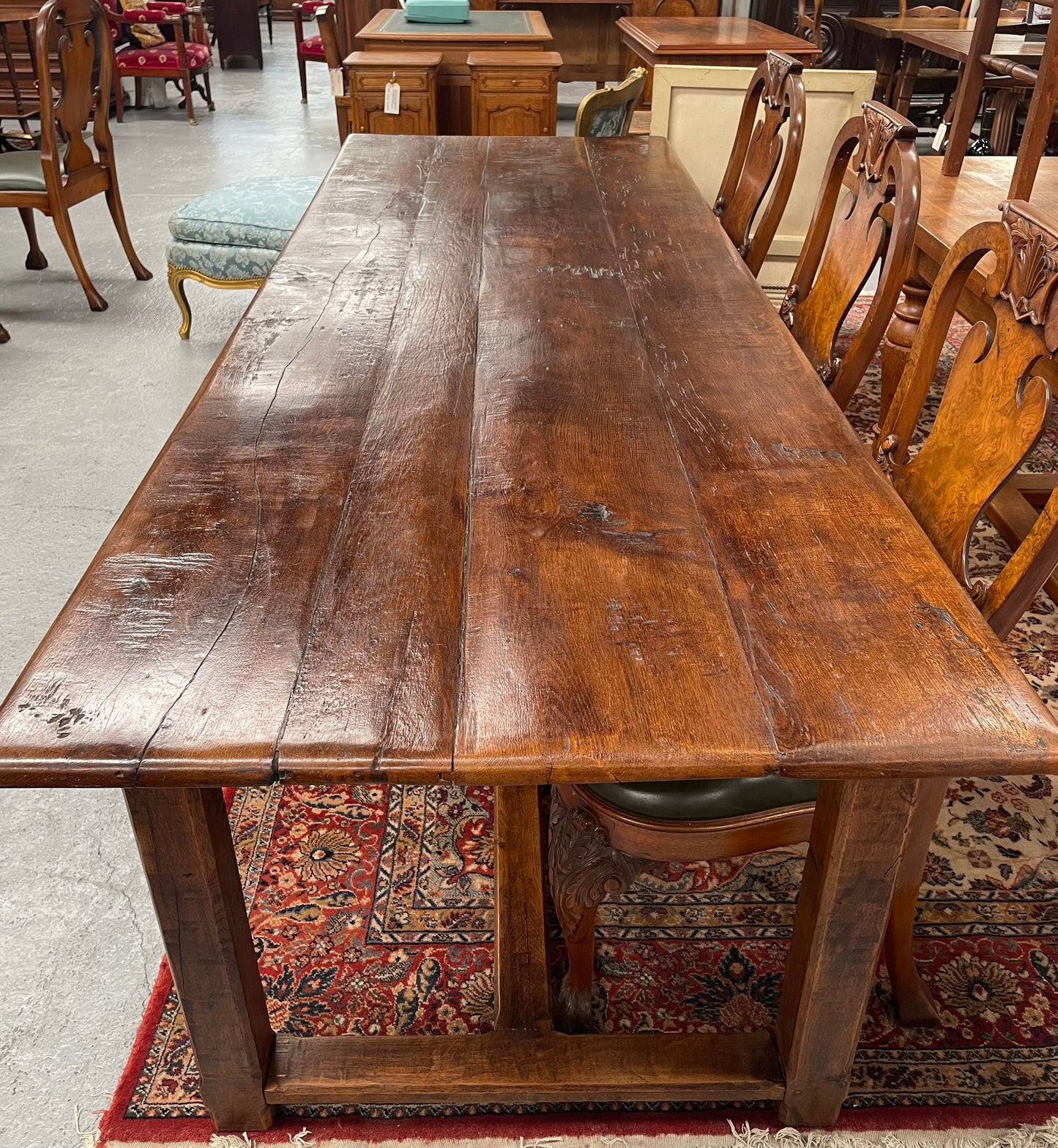 Rustic stretcher base dining table. The top consists of four heavy planks of French Oak timber. The surface is rustic and a little uneven and would require the use of place mats to even out. Please see photos as they form part of the description.