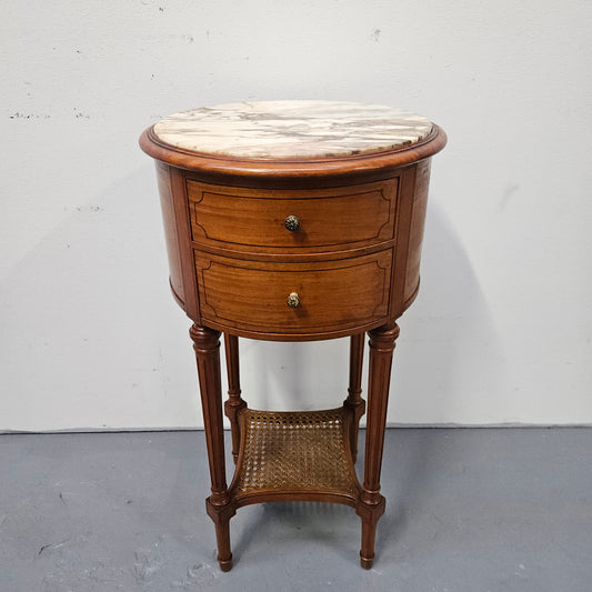 Charming Louis XVI style round side table. Features two drawers, fitted marble top and fluted legs connected by a cane shelf. Sourced directly from France and is in good original  detailed condition.