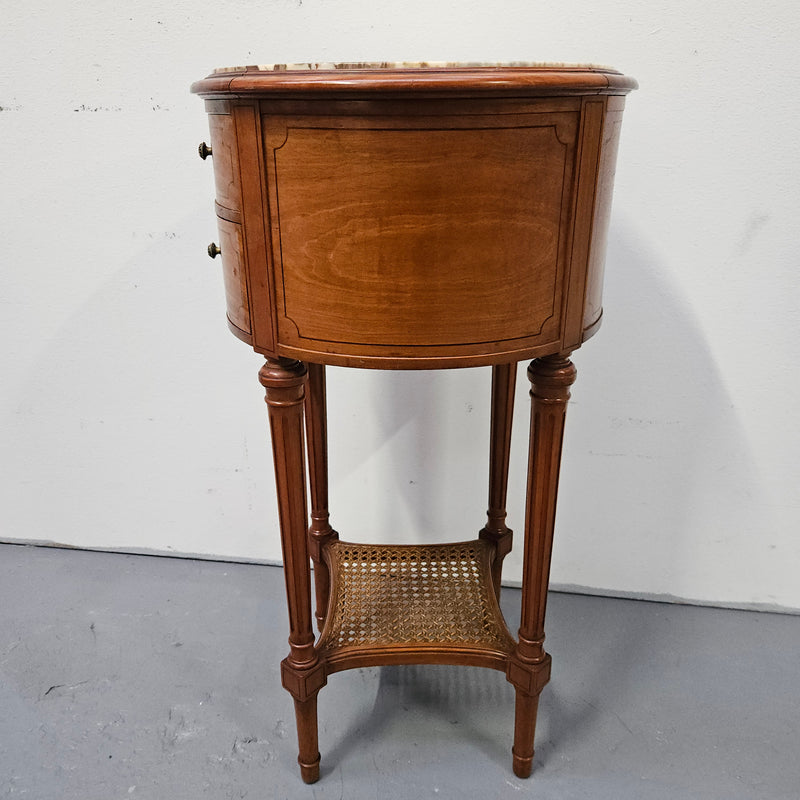 Charming Louis XVI style round side table. Features two drawers, fitted marble top and fluted legs connected by a cane shelf. Sourced directly from France and is in good original detailed condition.