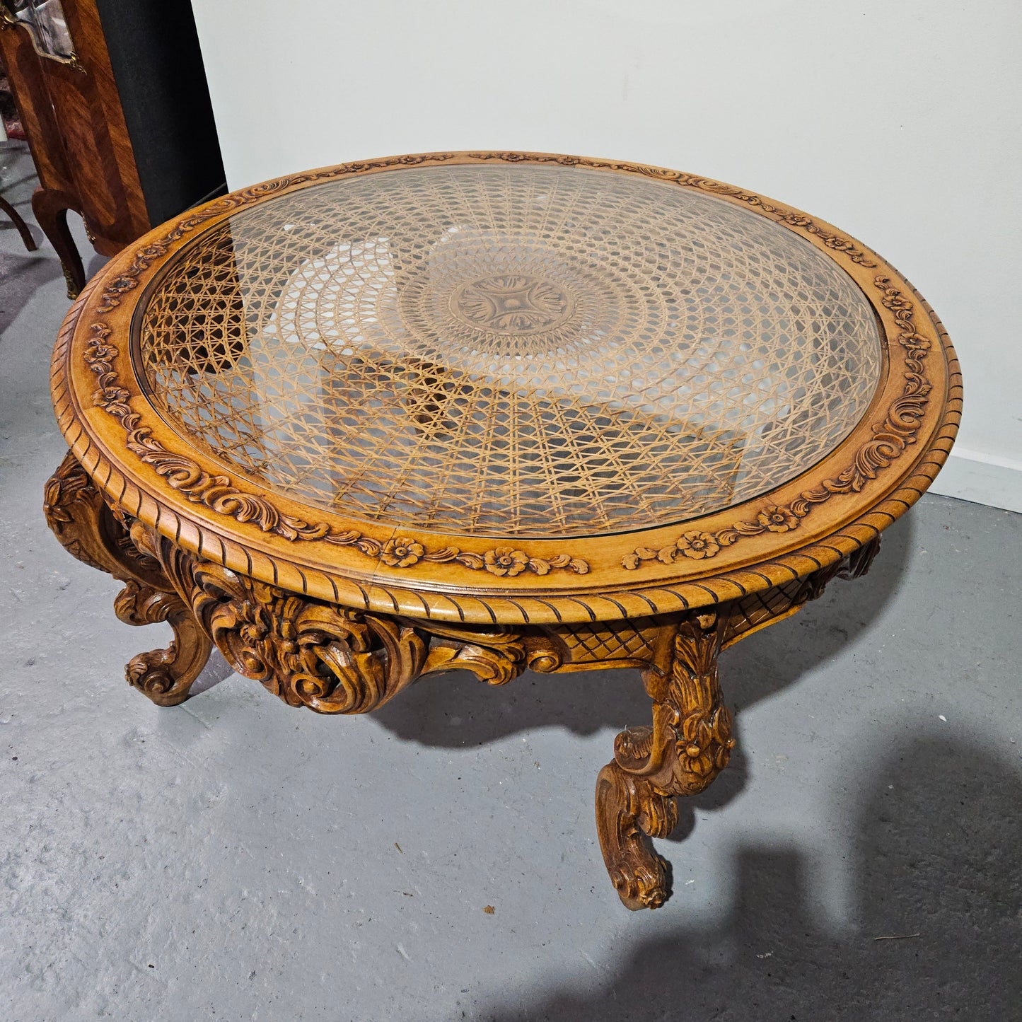 French oak Louis XV style round cane insert coffee table with highly decorative legs and table top. It has a glass cover to fit over the cane. It is in good original condition and has been sourced from France.