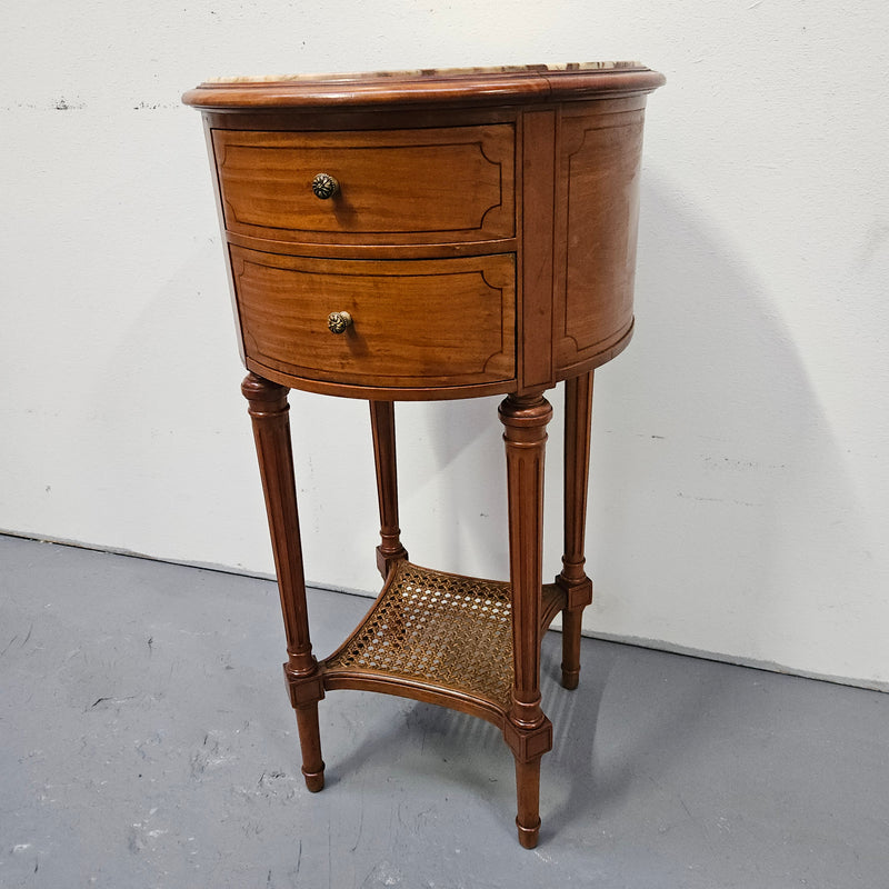 Charming Louis XVI style round side table. Features two drawers, fitted marble top and fluted legs connected by a cane shelf. Sourced directly from France and is in good original detailed condition.