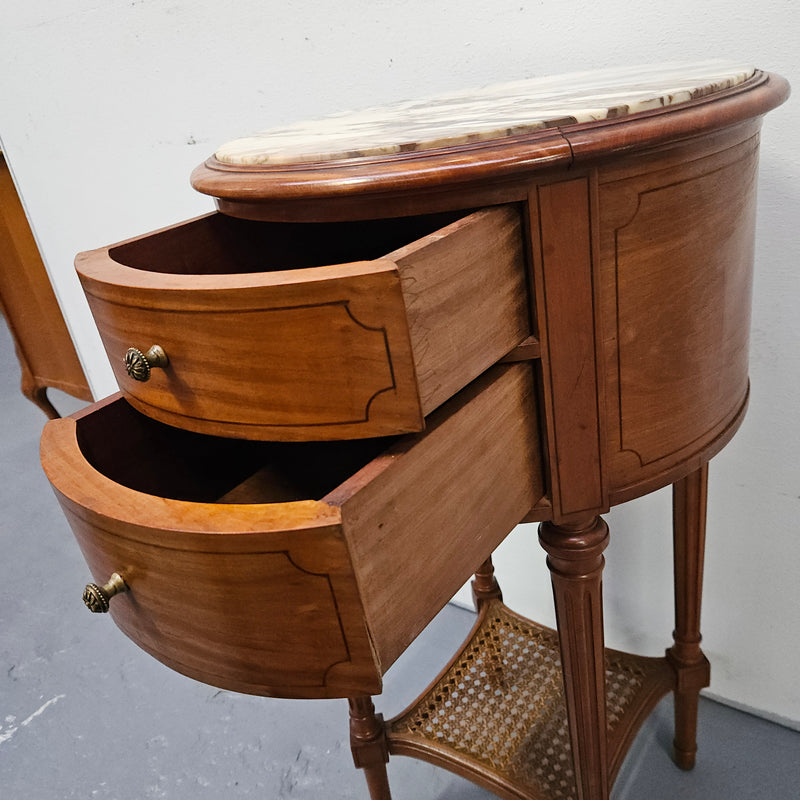 Charming Louis XVI style round side table. Features two drawers, fitted marble top and fluted legs connected by a cane shelf. Sourced directly from France and is in good original detailed condition.