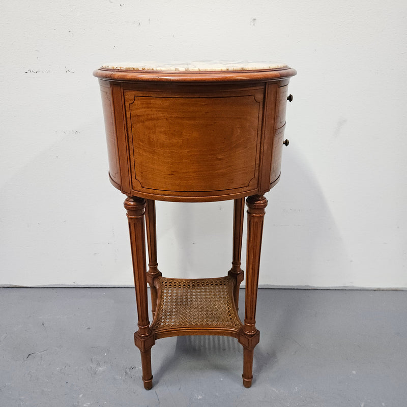 Charming Louis XVI style round side table. Features two drawers, fitted marble top and fluted legs connected by a cane shelf. Sourced directly from France and is in good original detailed condition.