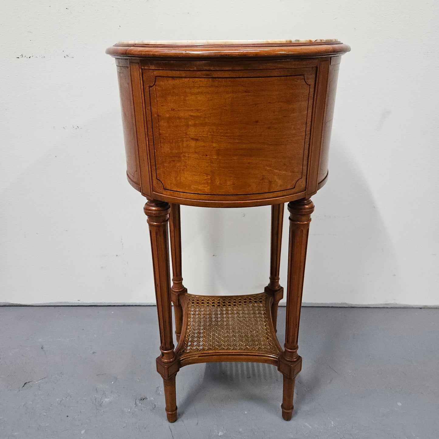 Charming Louis XVI style round side table. Features two drawers, fitted marble top and fluted legs connected by a cane shelf. Sourced directly from France and is in good original detailed condition.