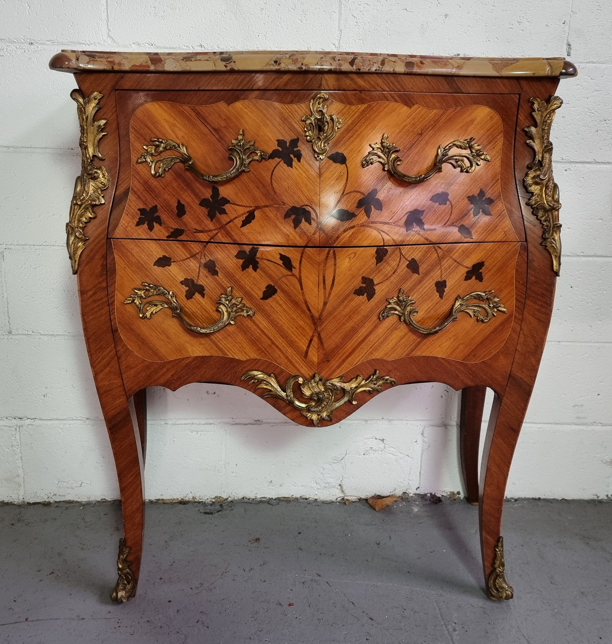 Charming petite French Louis XV style commode featuring two drawers, marquetry inlay, ormolu trim and marble Top. In good original detailed condition. Circa: 1930’s.