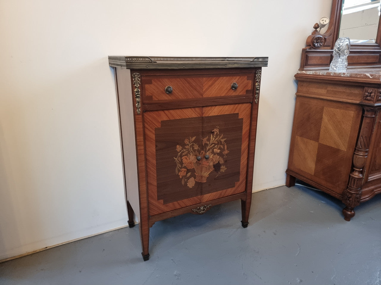 Louis 16th style marquetry inlaid side cabinet with a pierced brass gallery surrounding a marble top. It has two doors open up to storage with one shelf and a drawer above that. In good original detailed condition.