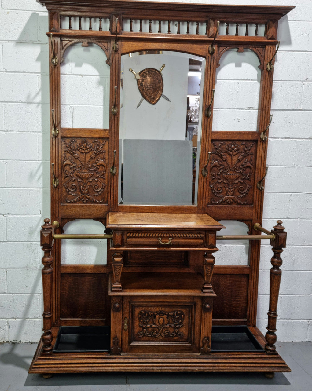 Grand Henry 2nd Style French Oak hall stand with 12 hanging hooks. Also has one cupboard and drawer for storage along with a mirror and two areas either side for umbrellas and walking sticks. In good original detailed condition.