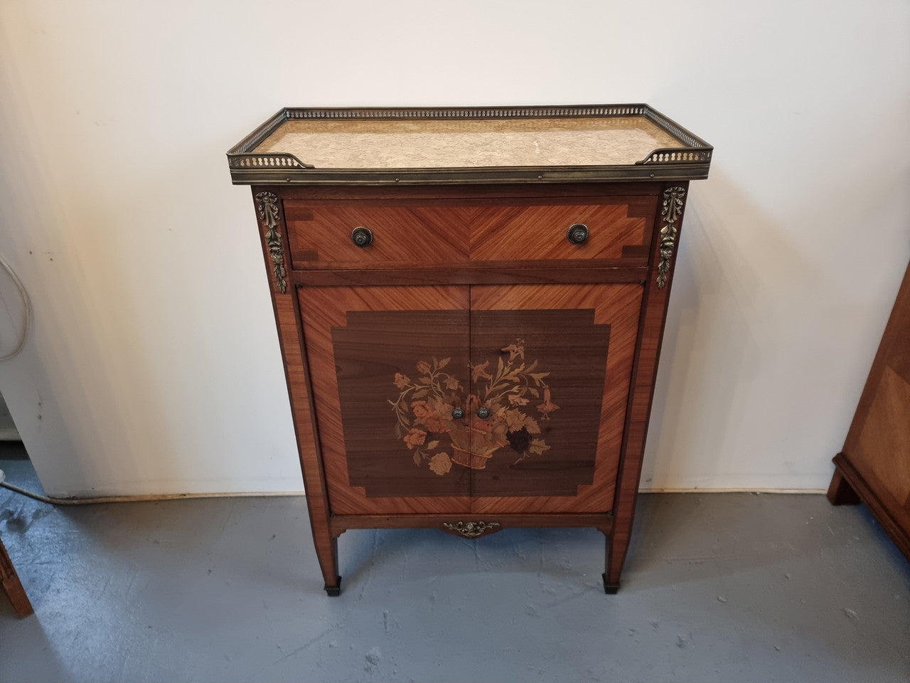 Louis 16th style marquetry inlaid side cabinet with a pierced brass gallery surrounding a marble top. It has two doors open up to storage with one shelf and a drawer above that. In good original detailed condition.