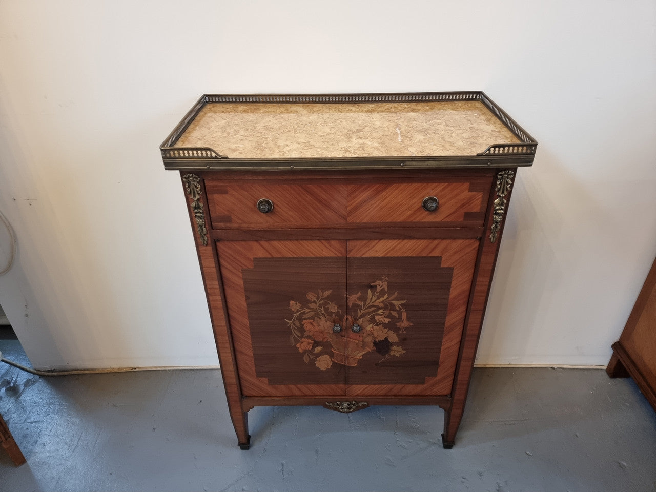 Louis 16th style marquetry inlaid side cabinet with a pierced brass gallery surrounding a marble top. It has two doors open up to storage with one shelf and a drawer above that. In good original detailed condition.