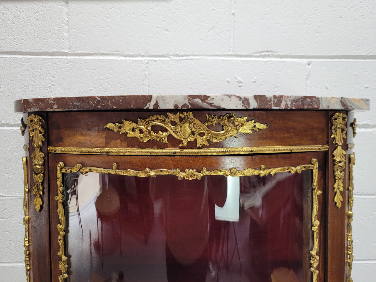 Louis XV style Vitrine with curved glass and red velvet lining. It has two fixed shelves with a marble top and ormolu decoration. In good original detailed condition.