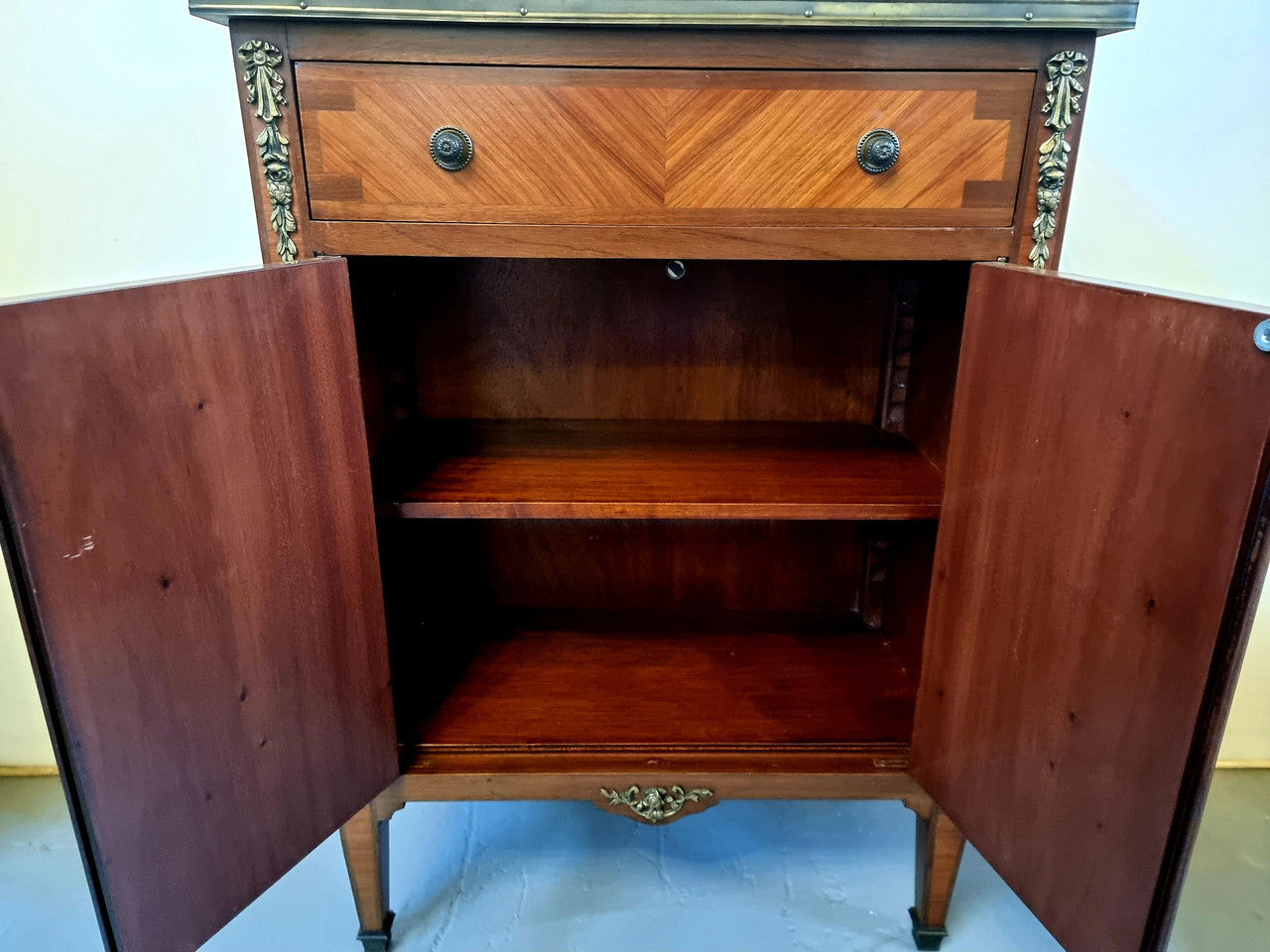 Louis 16th style marquetry inlaid side cabinet with a pierced brass gallery surrounding a marble top. It has two doors open up to storage with one shelf and a drawer above that. In good original detailed condition.