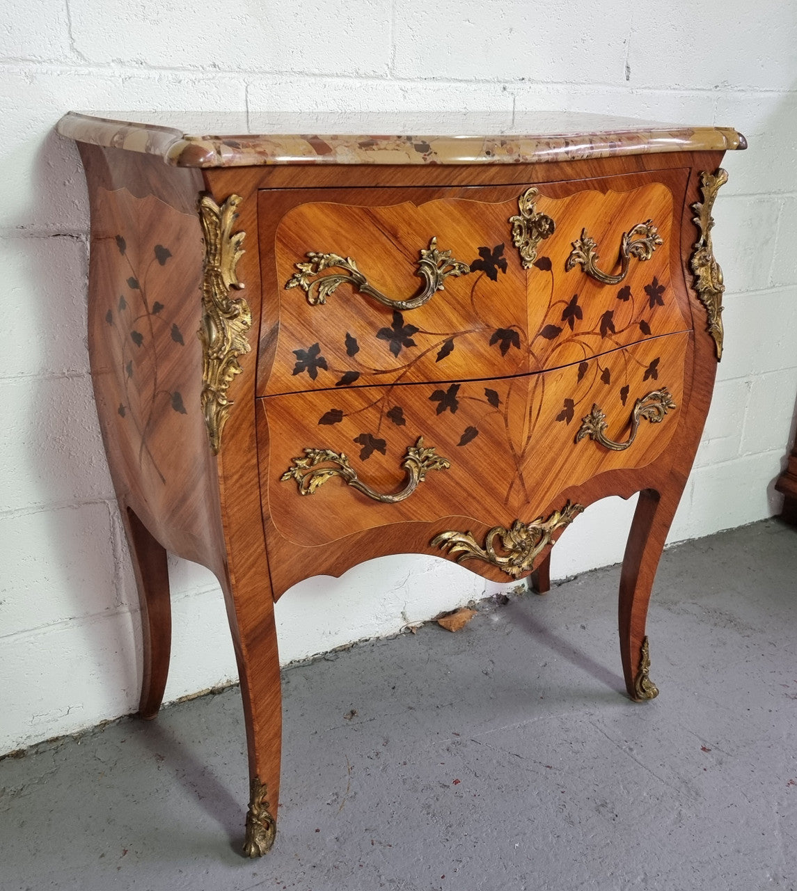 Charming petite French Louis XV style commode featuring two drawers, marquetry inlay, ormolu trim and marble Top. In good original detailed condition. Circa: 1930’s.