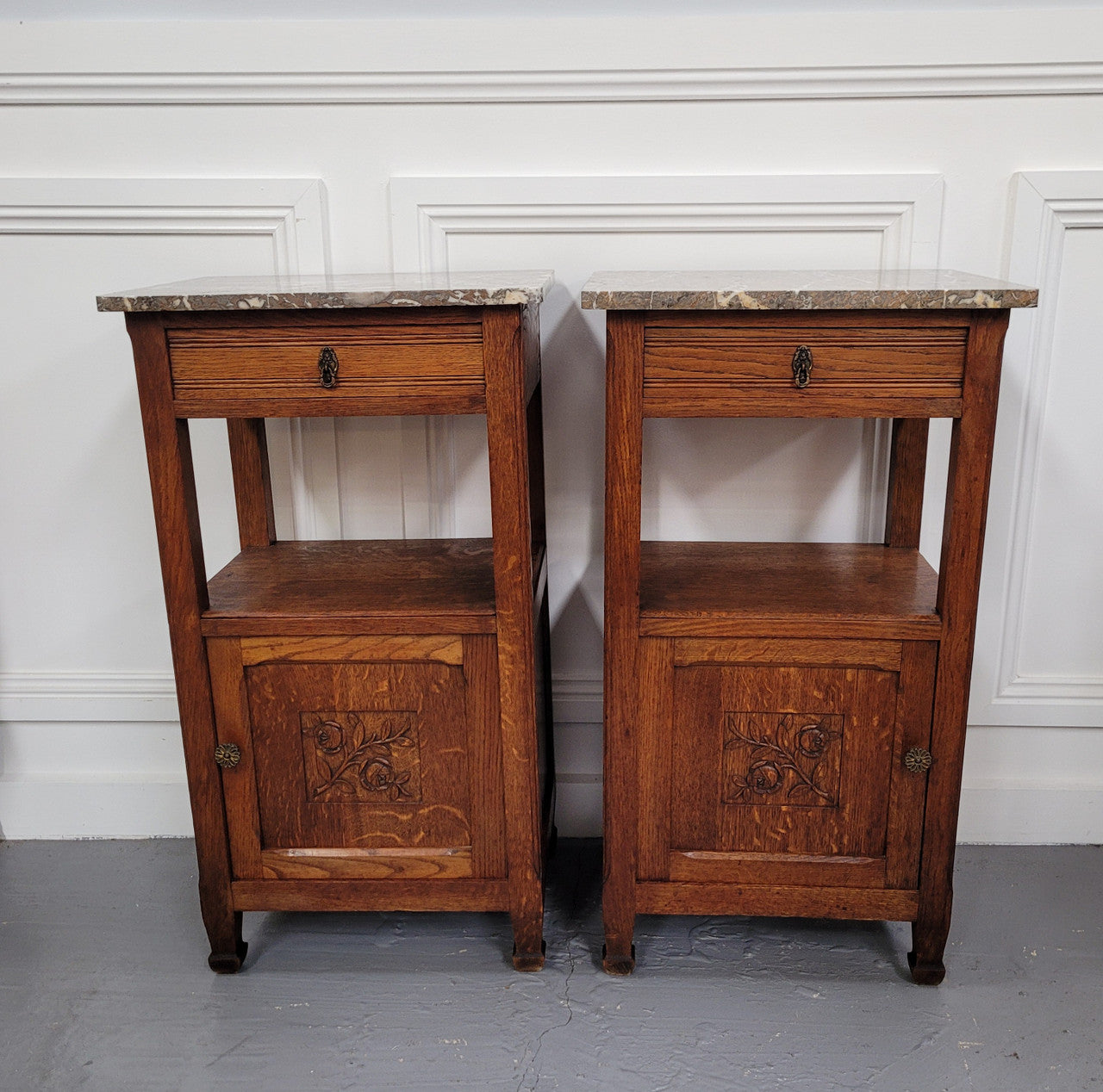 Pair of French Oak Arts & Crafts style marble top bedside cabinets. They have lovely carvings on the door, an open shelf in the middle and drawer at the top. They are in good original detailed condition.