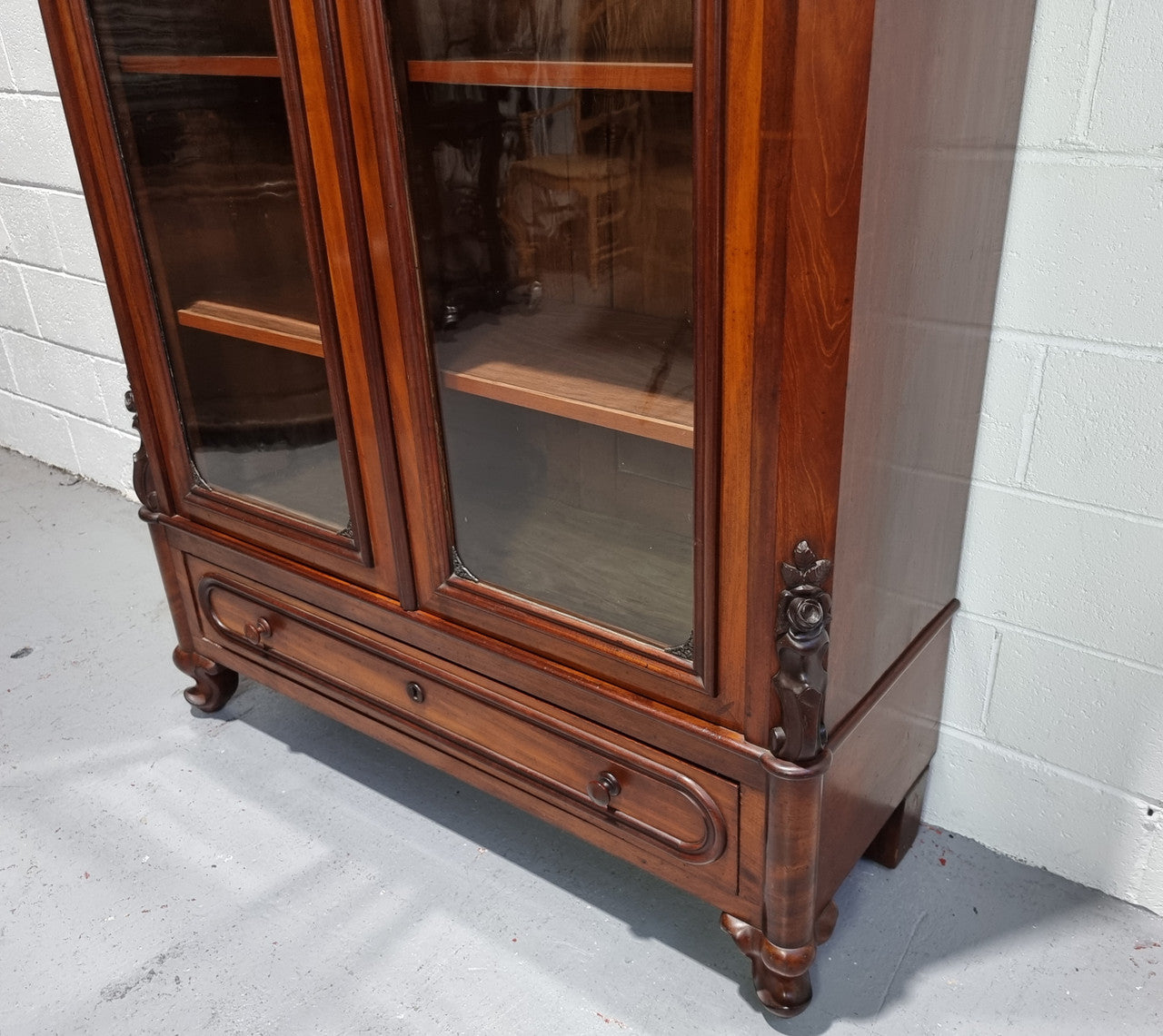 Antique Mahogany two door Biedermeier style bookcase with four fully adjustable shelves and a drawer at the bottom. The two wooden finials at the top are easily removed for a different look of desired. In good original detailed condition.