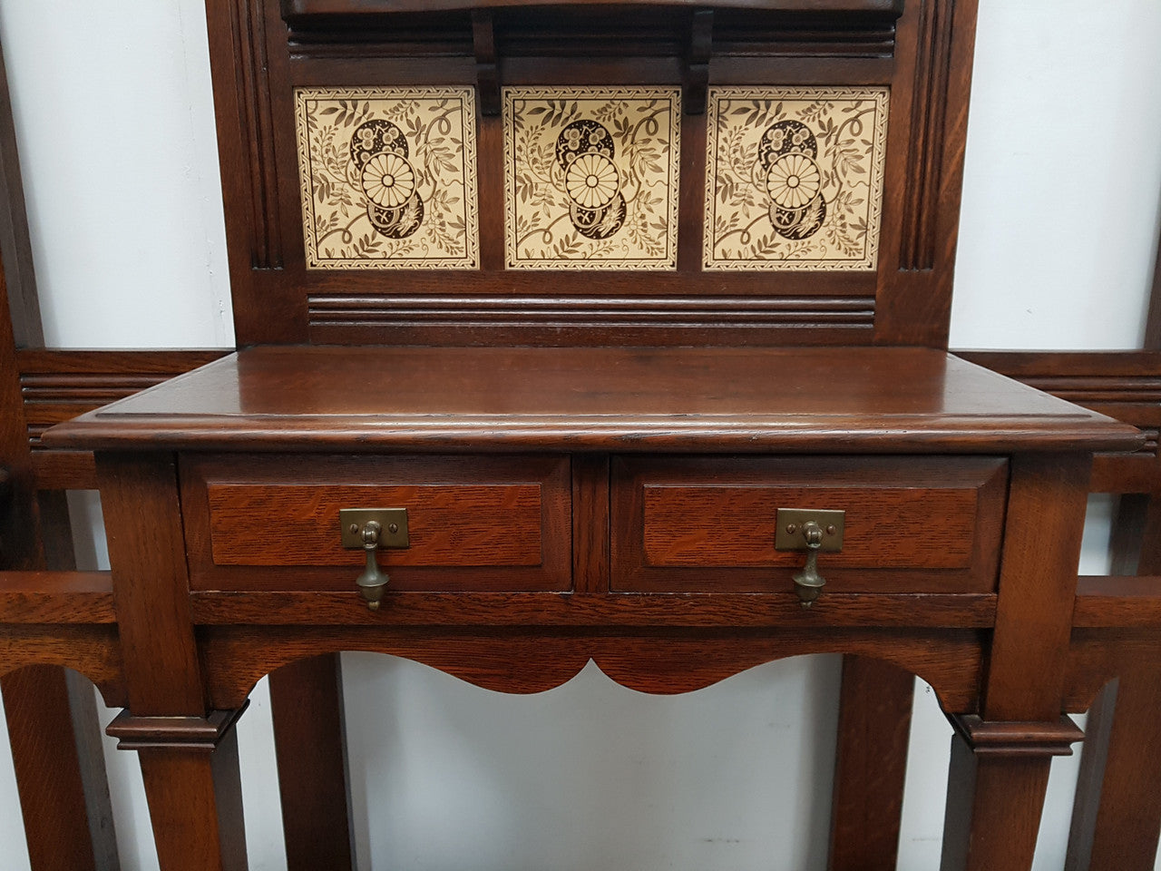 Beautiful English Edwardian tiled back hall stand, with nine brass hooks, two small drawers and retaining it's original mirror and showing signs of age. In good original condition.