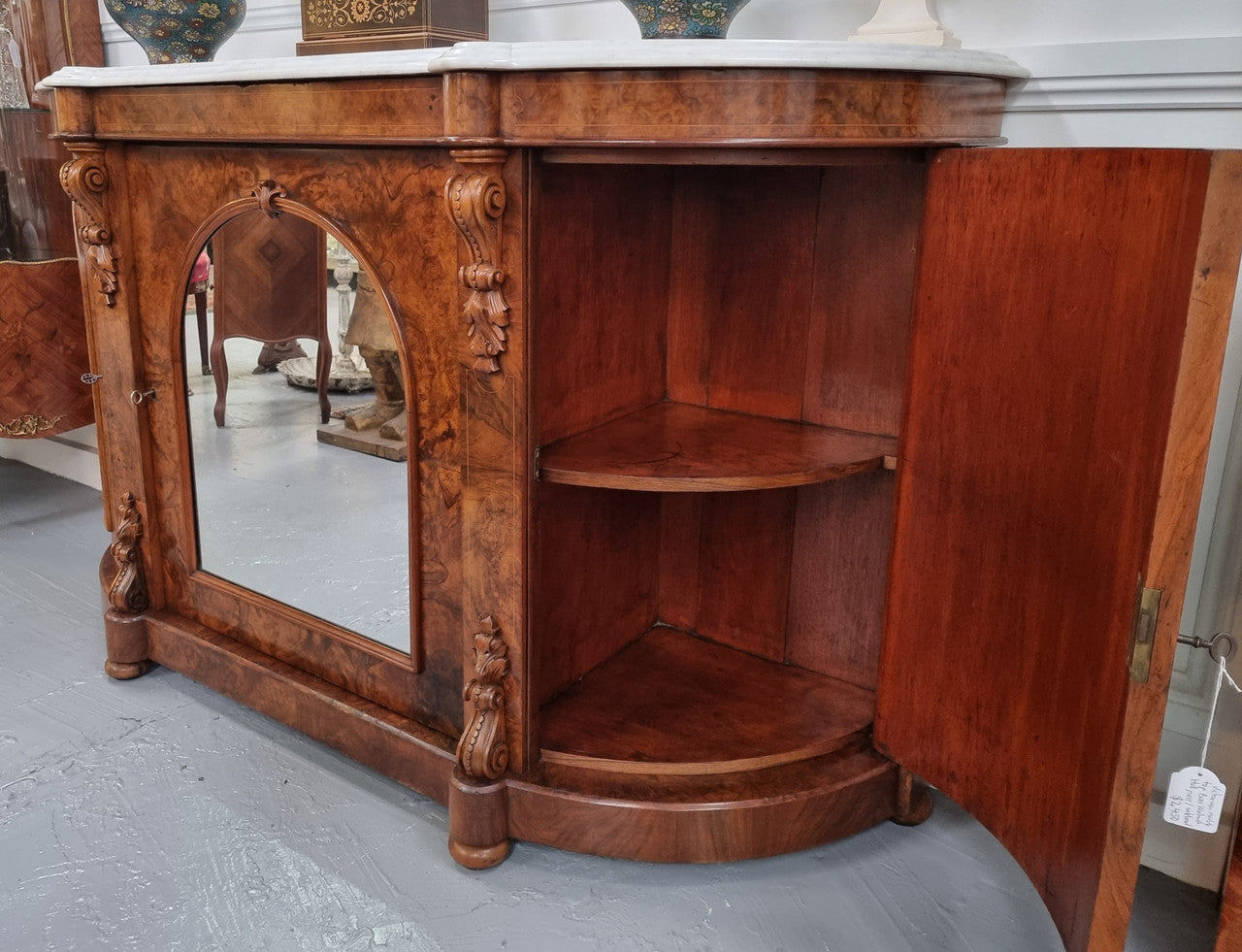 An elegant Antique Victorian Burr wood Walnut marble-top sideboard credenza with a mirrored center door. It has a white shaped marble top, mirror front, nicely carved details and three swing doors along with two keys. It is in good original detailed condition.