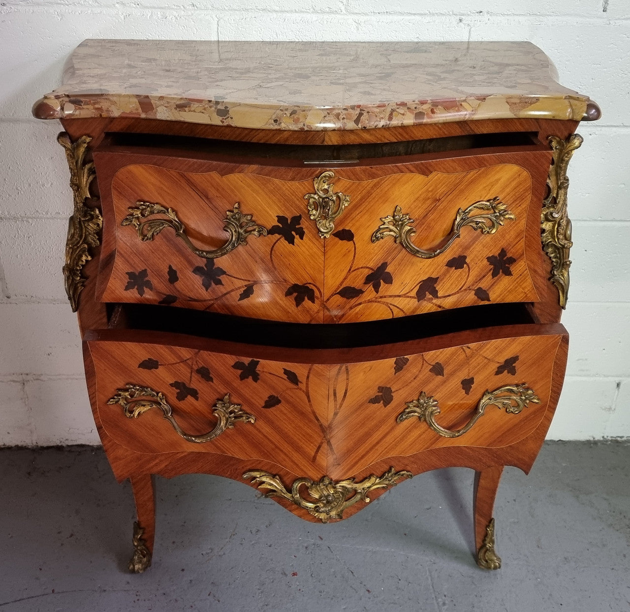 Charming petite French Louis XV style commode featuring two drawers, marquetry inlay, ormolu trim and marble Top. In good original detailed condition. Circa: 1930’s.