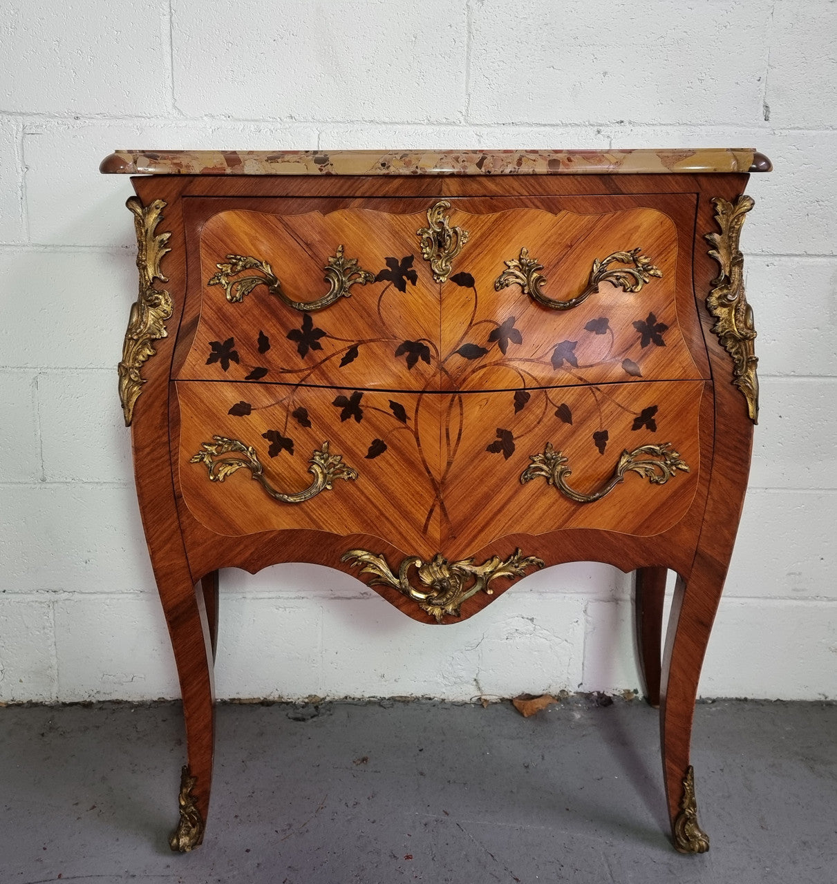 Charming petite French Louis XV style commode featuring two drawers, marquetry inlay, ormolu trim and marble Top. In good original detailed condition. Circa: 1930’s.