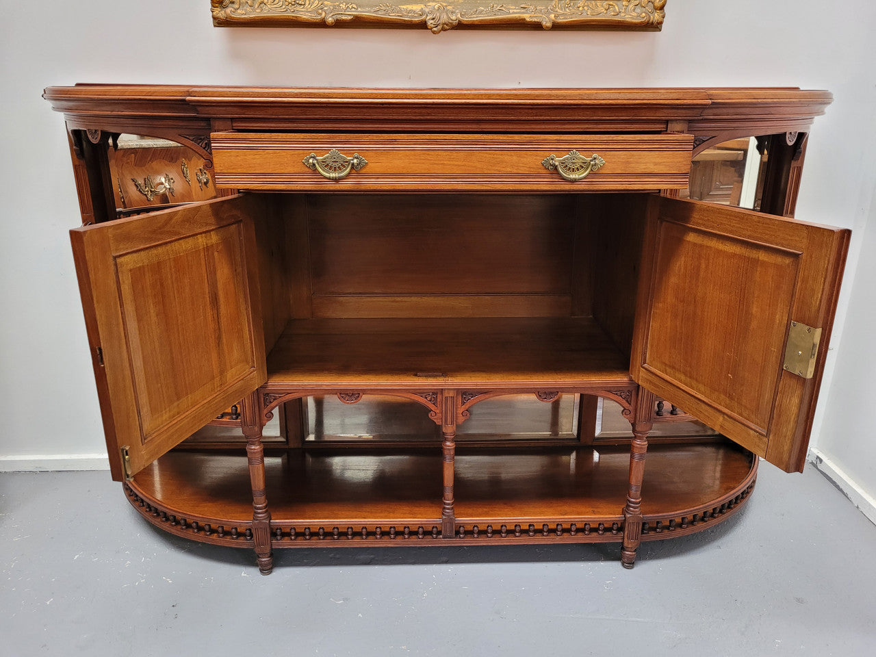 A high quality Antique Walnut sideboard featuring two mirrored doors, two drawers and five open shelf areas with mirror backing. It is in good original detailed condition.