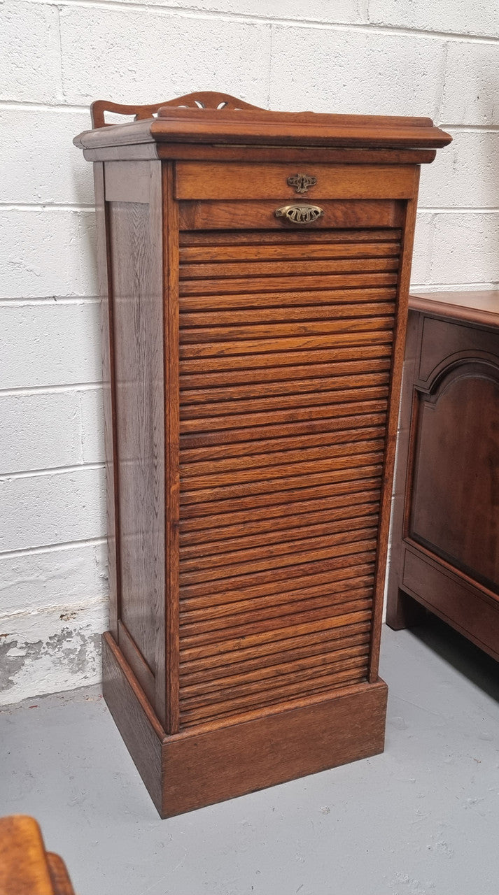Antique Edwardian roll top Tambour file cabinet desk. This practical antique tambour front filing cabinet dates around 1900 in the Edwardian period and is constructed from Oak. This antique cabinet has an adjustable writing slope, above a tambour front with key and working lock. It has been sourced locally and is in good original detailed condition.