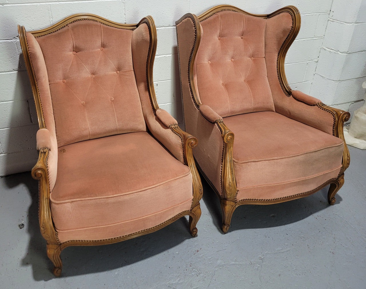French pair of Walnut Louis XV style pink upholstered wing back chairs. They are very comfortable to sit in and are of generous portions. The fabric is in good original condition and does have stains and would ideally be reupholstered.