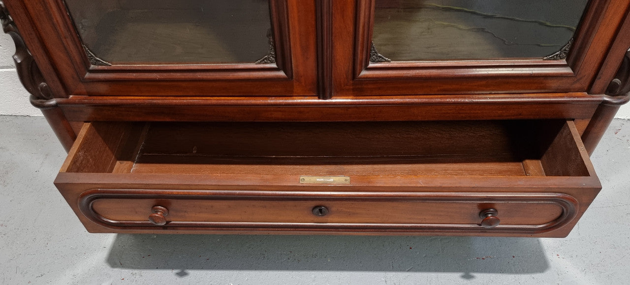 Antique Mahogany two door Biedermeier style bookcase with four fully adjustable shelves and a drawer at the bottom. The two wooden finials at the top are easily removed for a different look of desired. In good original detailed condition.