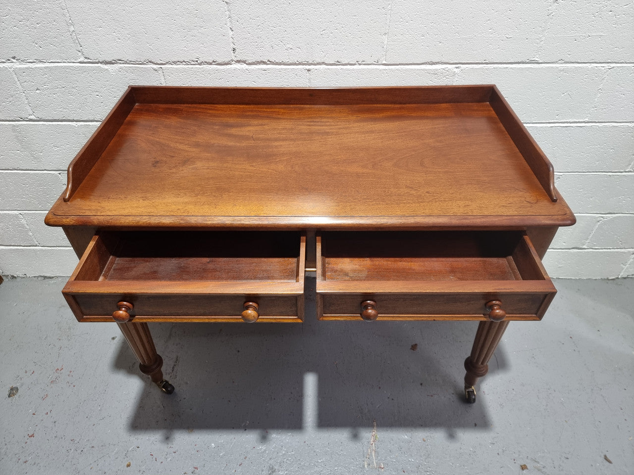 English Victorian Mahogany side table or desk with two drawers and gallery, fluted legs and ceramic castors. In good original condition.