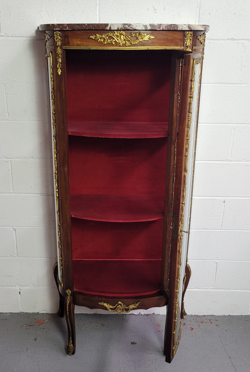 Louis XV style Vitrine with curved glass and red velvet lining. It has two fixed shelves with a marble top and ormolu decoration. In good original detailed condition.