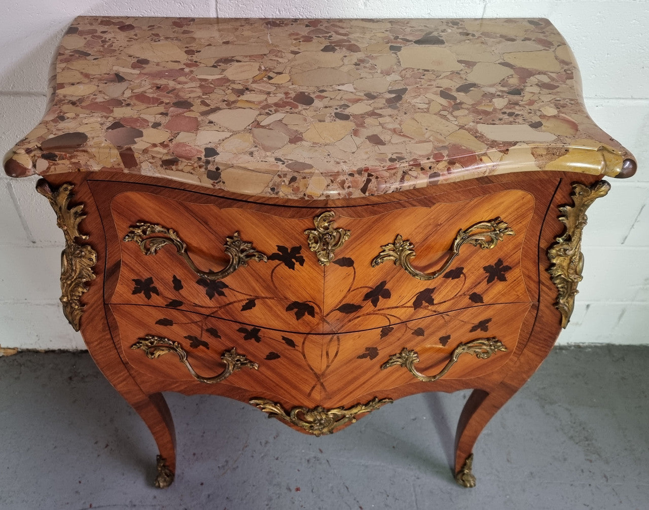 Charming petite French Louis XV style commode featuring two drawers, marquetry inlay, ormolu trim and marble Top. In good original detailed condition. Circa: 1930’s.