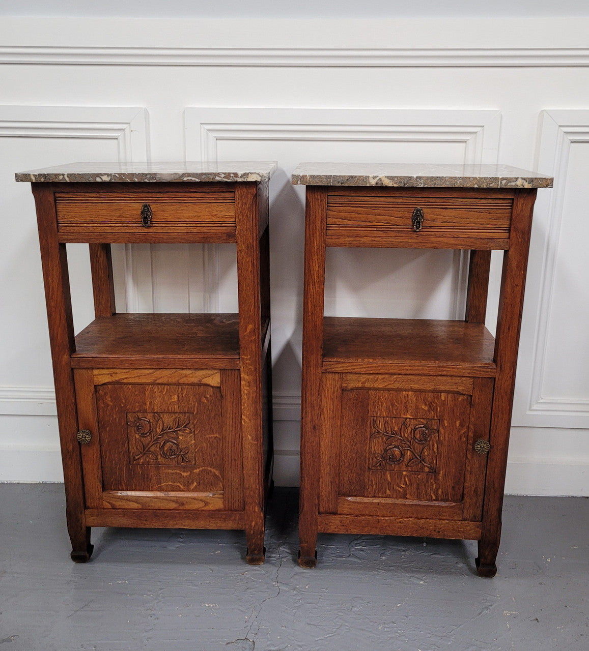 Pair of French Oak Arts & Crafts style marble top bedside cabinets. They have lovely carvings on the door, an open shelf in the middle and drawer at the top. They are in good original detailed condition.