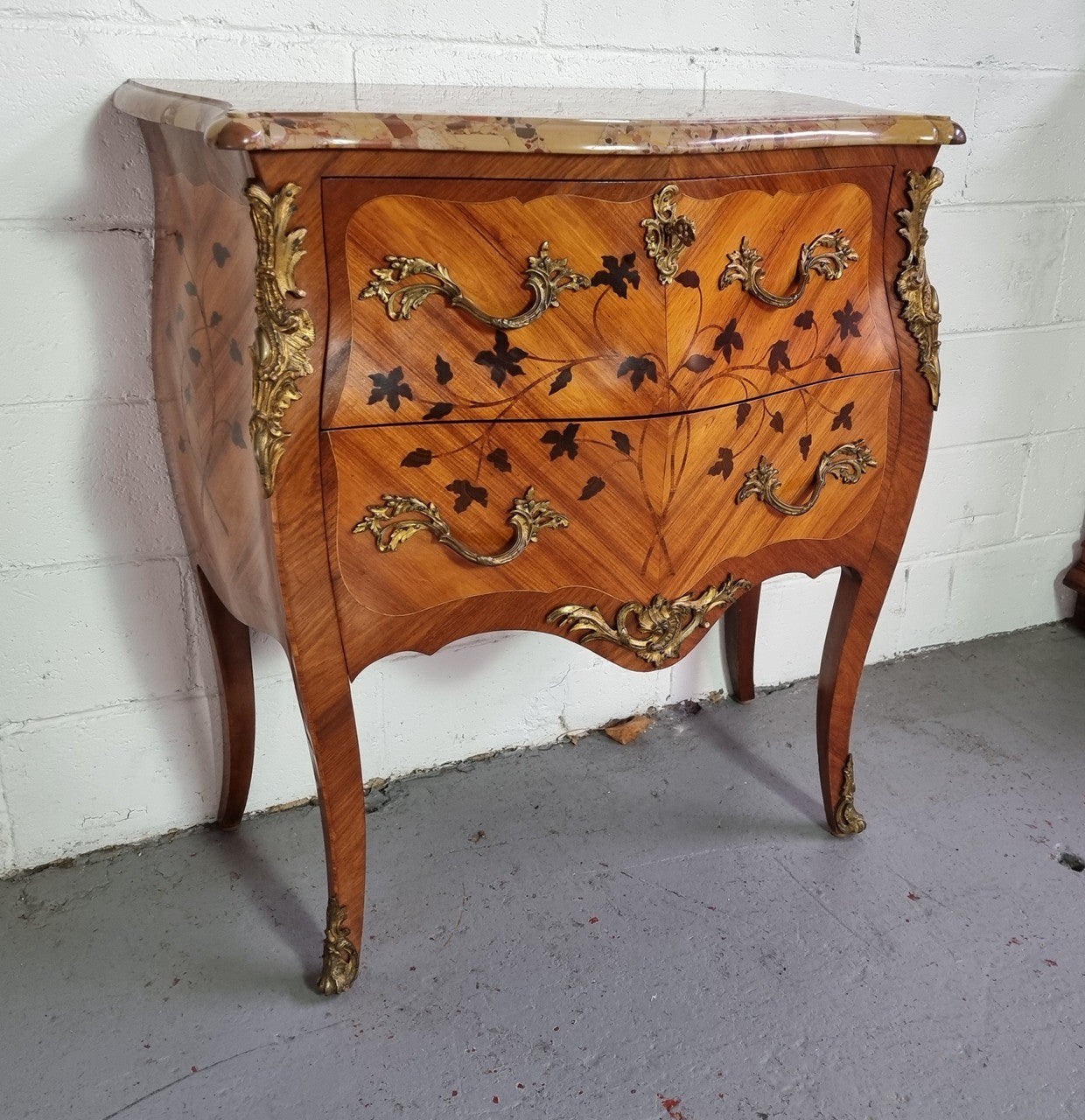 Charming petite French Louis XV style commode featuring two drawers, marquetry inlay, ormolu trim and marble Top. In good original detailed condition. Circa: 1930’s.