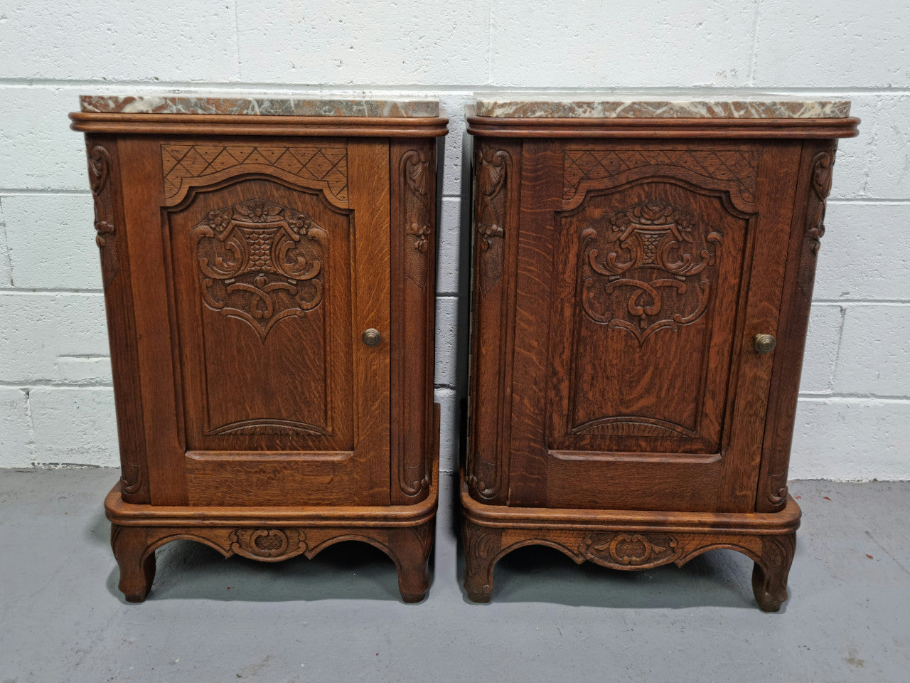 Lovely pair of French oak bedside cabinets with nicely carved details and marble tops. In good original detailed condition.