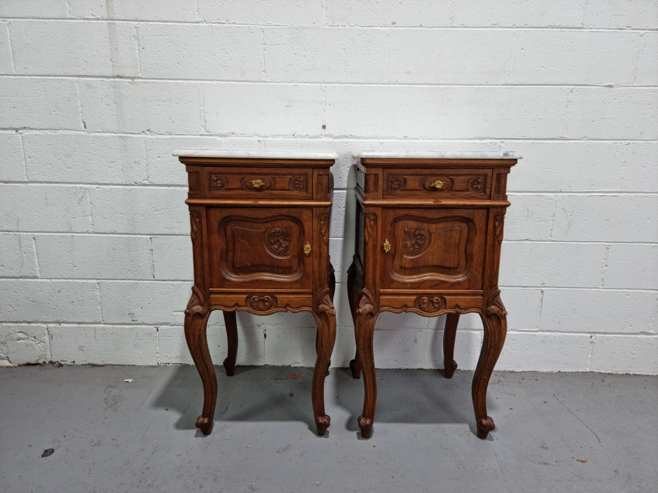 Lovely pair of French Oak carved Louis XV style bedside cabinets with a white marble top, drawer and cupboard in good original detailed condition.