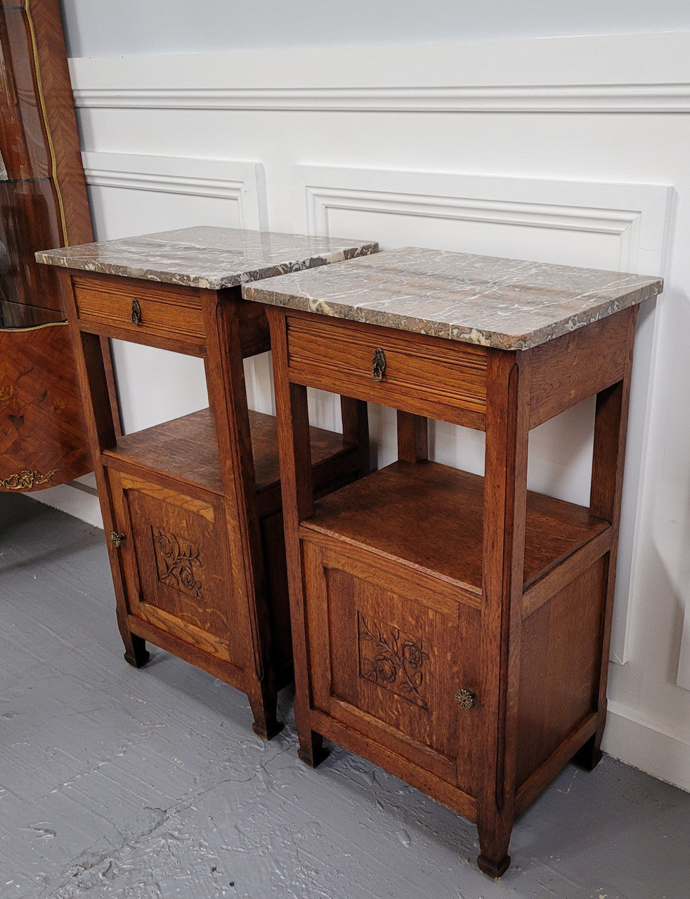 Pair of French Oak Arts & Crafts style marble top bedside cabinets. They have lovely carvings on the door, an open shelf in the middle and drawer at the top. They are in good original detailed condition.
